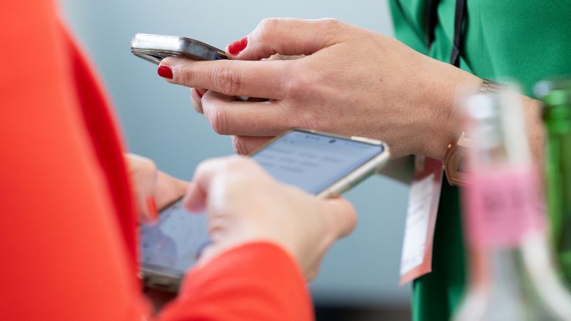 Nahaufnahme von zwei Frauen, die jeweils ein Handy in der Hand halten, um ihre Kontaktdaten auszutauschen.